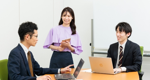 三人がテーブルに集まり、ノートパソコンで作業しているシーン。