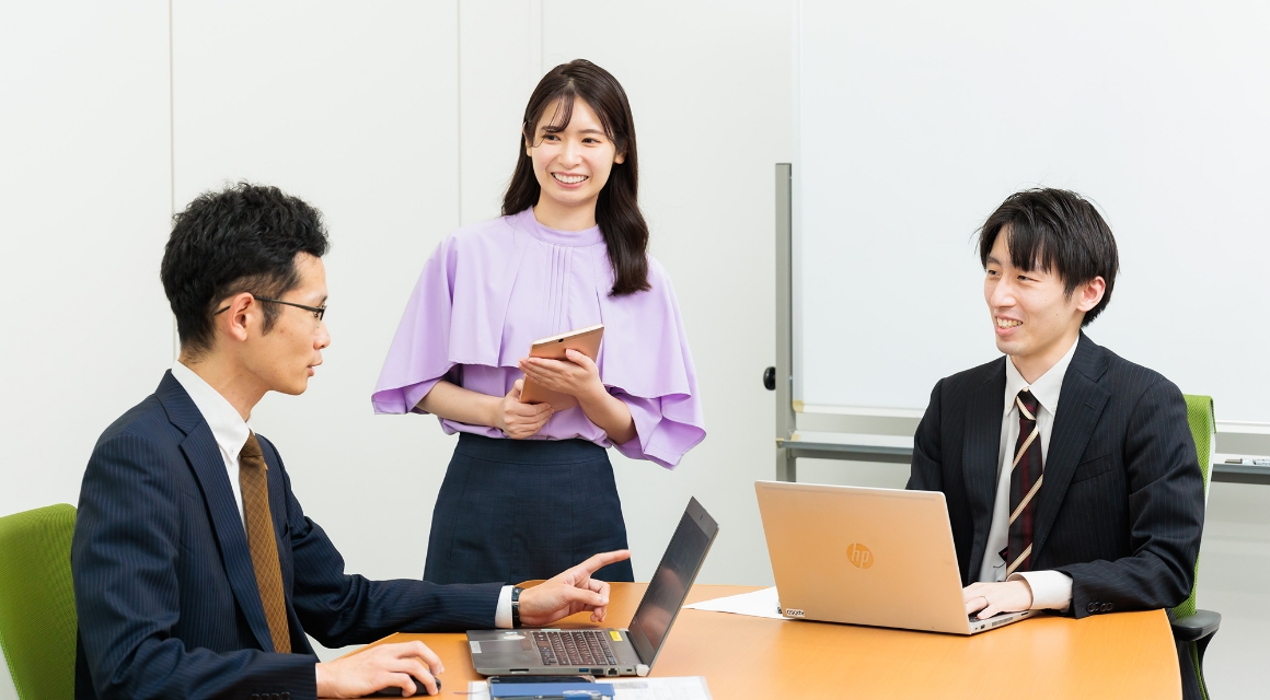 三人がテーブルに集まり、ノートパソコンで作業しているシーン。