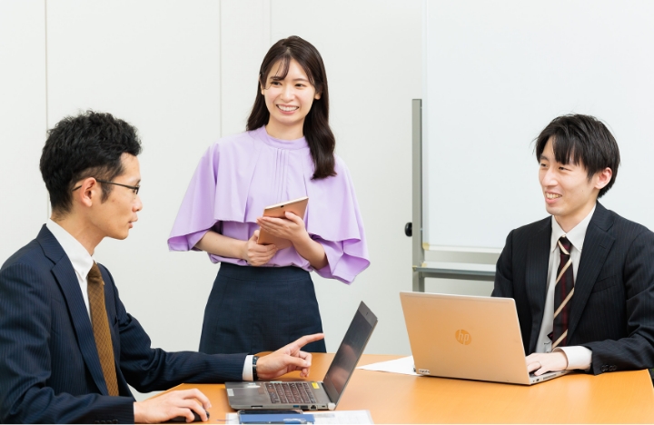 三人がテーブルに集まり、ノートパソコンで作業しているシーン。
