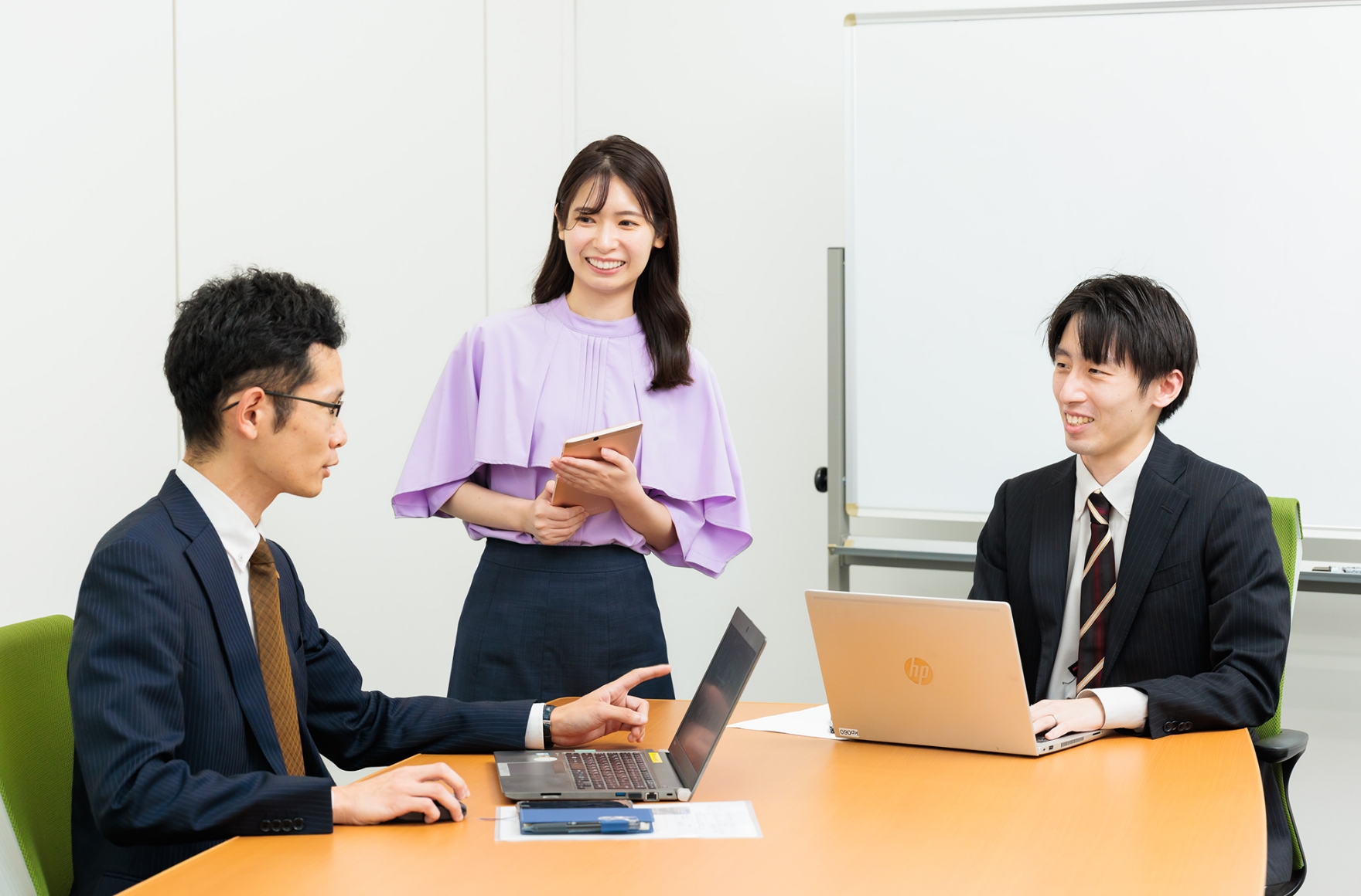 三人がテーブルに集まり、ノートパソコンで作業しているシーン。