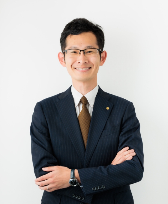 腕を組んで立つスーツ姿の男性。自信に満ちた表情。