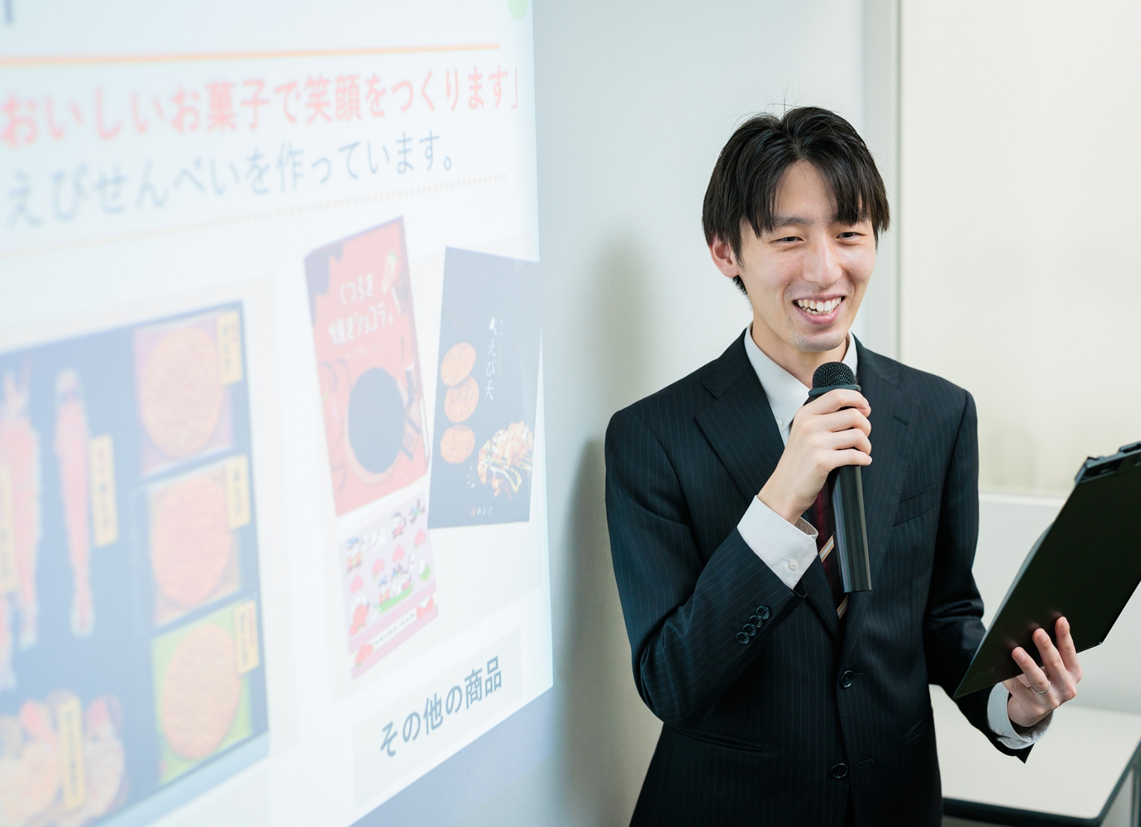 マイクを持つスーツ姿の男性が写っています。