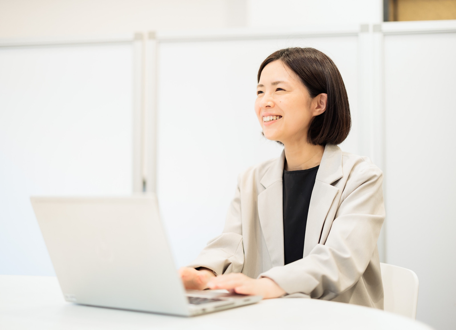 アジア系女性がオフィスでノートパソコンに向かっている様子。
