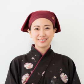 黒と赤の着物を着た女性が微笑んでいる様子を捉えた画像です。