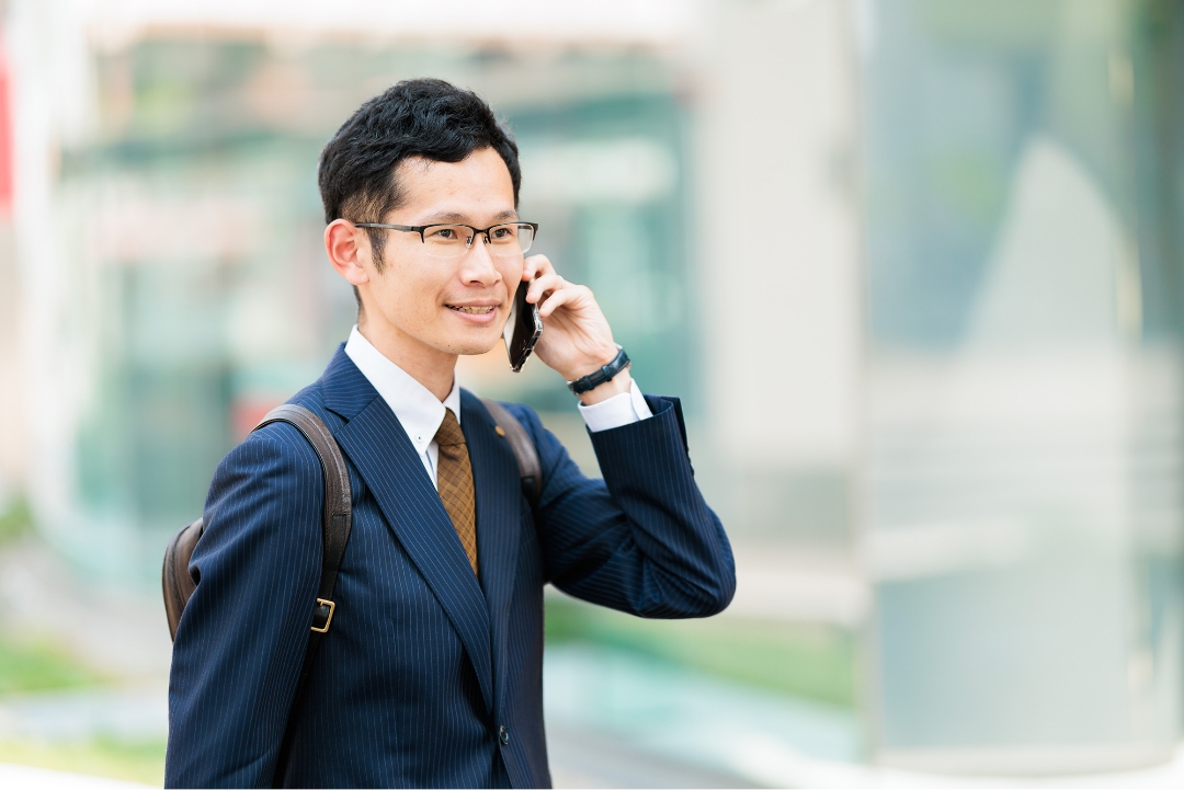 電話を持ちながら都市の中で話しているアジア系のビジネスマン。