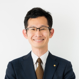 スーツ姿の男性がカメラに向かって笑顔を見せている。